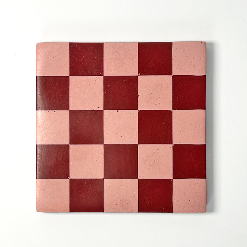 Dark red and pink checkerboard patterned coaster on a white background