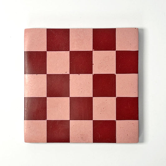 Dark red and pink checkerboard patterned coaster on a white background