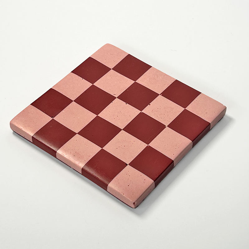 Dark red and pink checkerboard patterned coaster on a white background