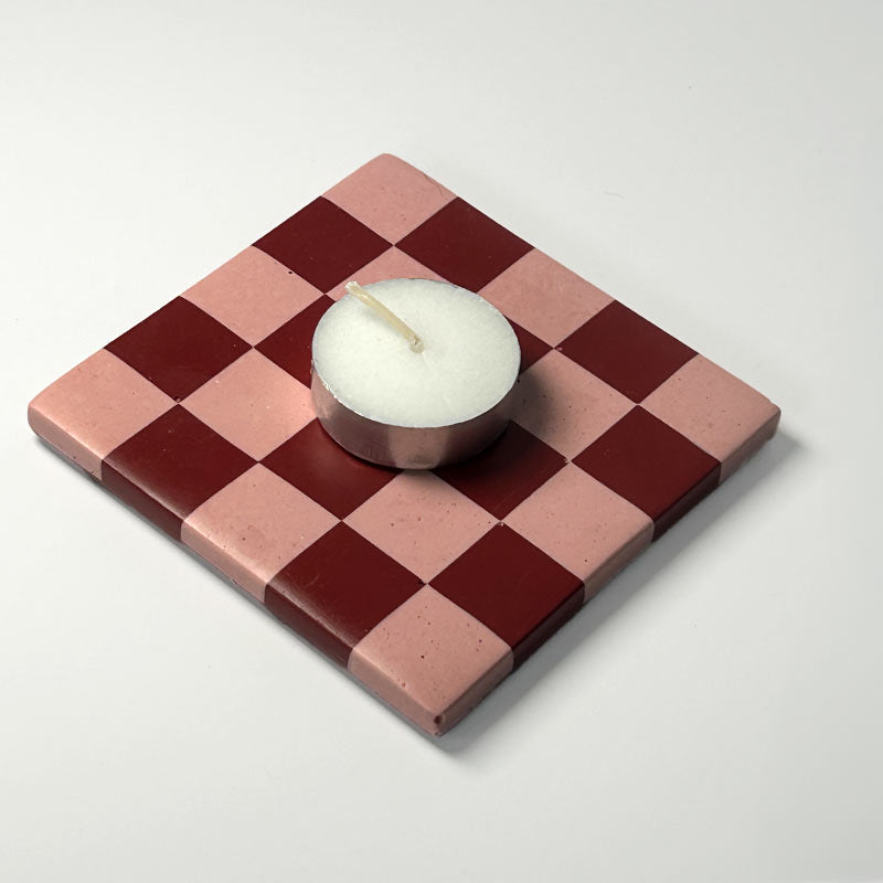 Dark red and pink checkered coaster with a white tea light candle on a white 
background