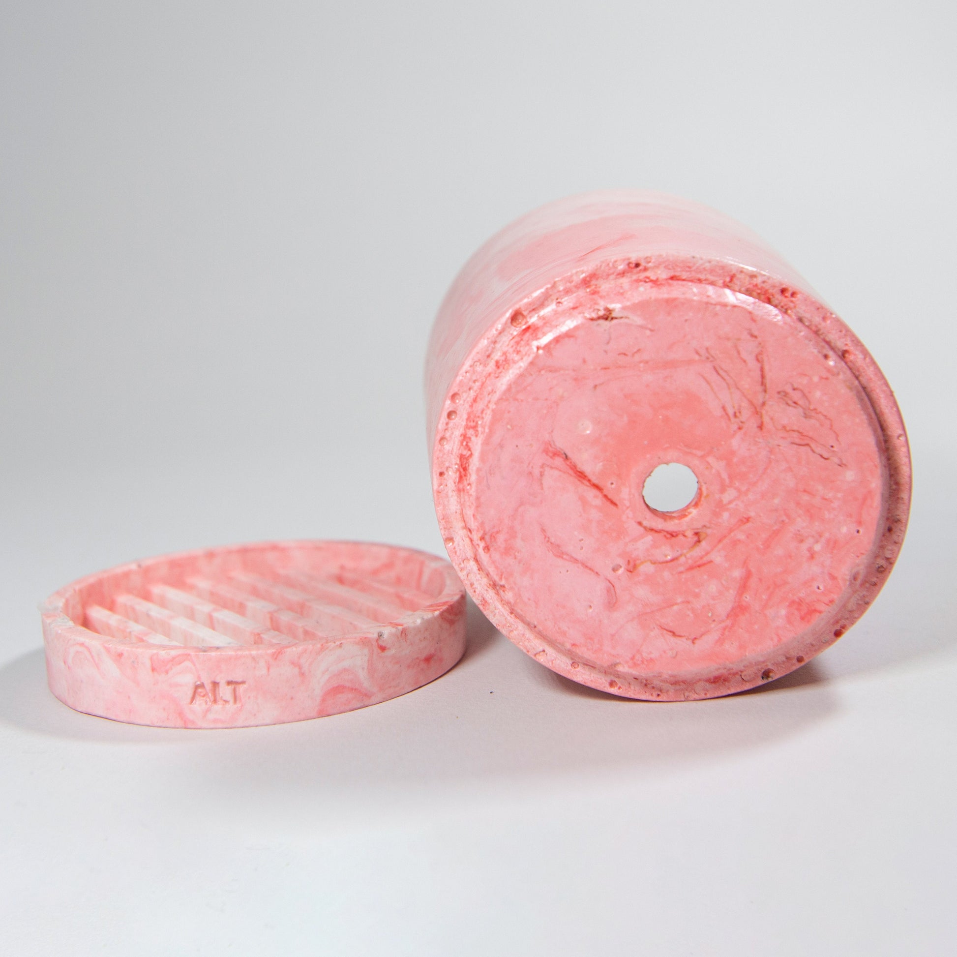 Pink marbled cylindrical plant pot with a drainage and a water tray on a grey background