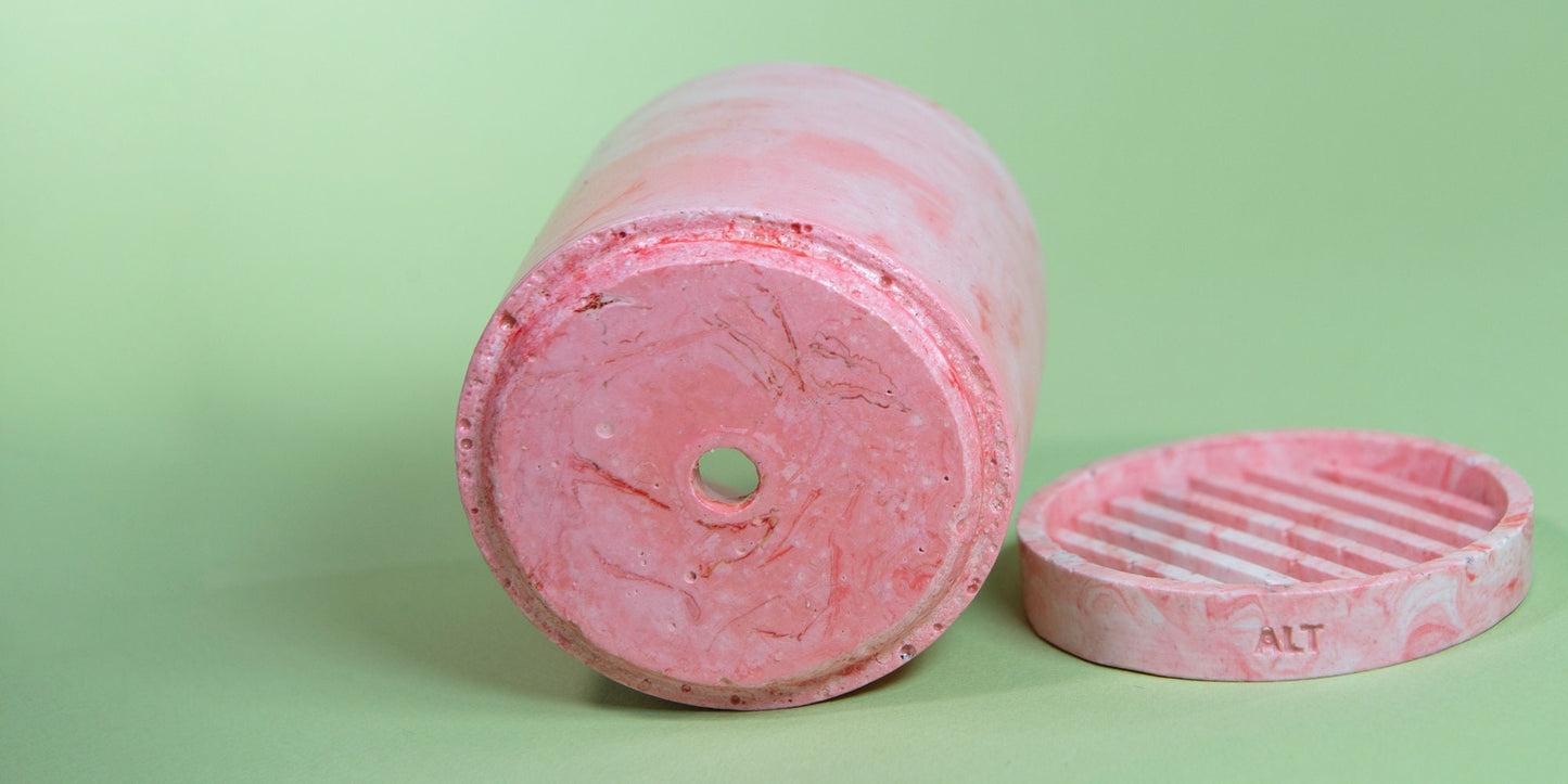 Pink marbled cylindrical plant pot with a drainage and a water tray on green background 