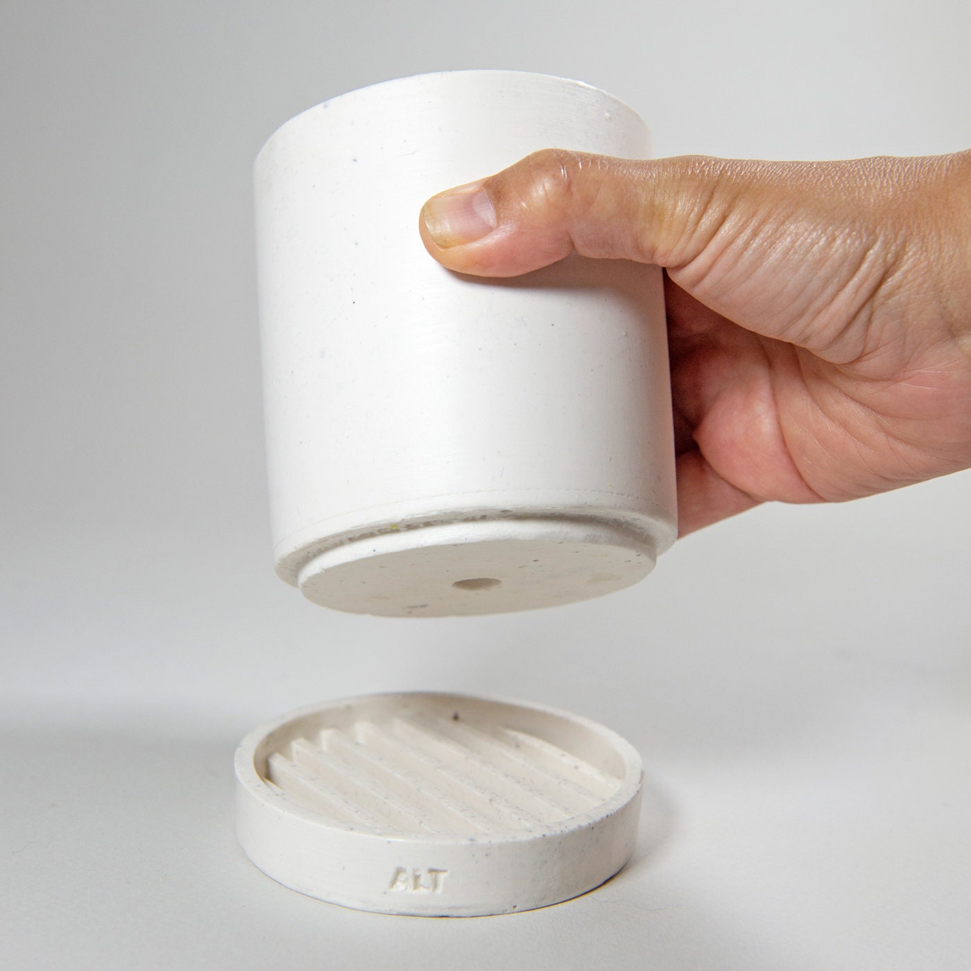 Hand holding a white Jesmonite container with a separate water tray on a light gray background