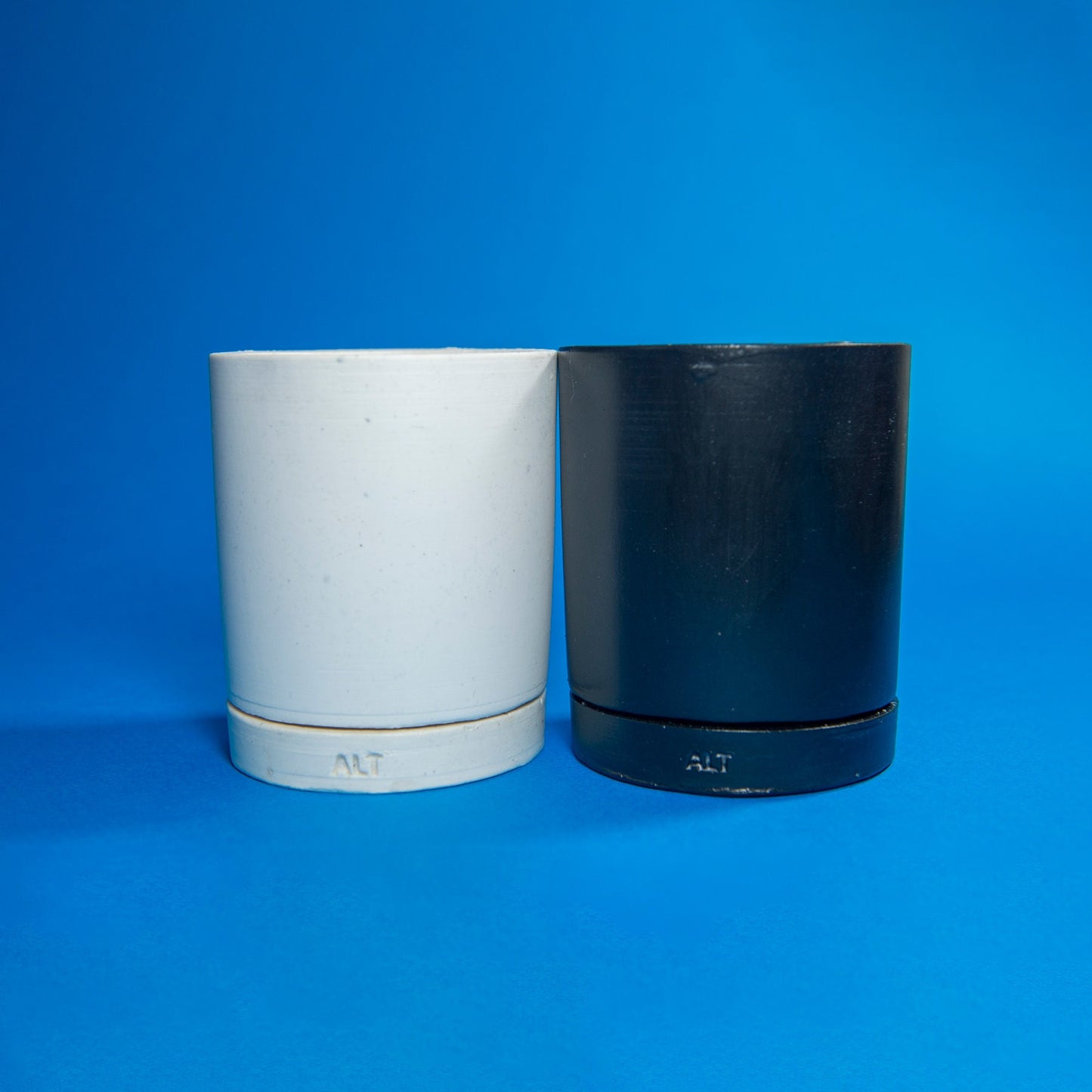 Two cylindrical containers, one white and one black, on a blue background.