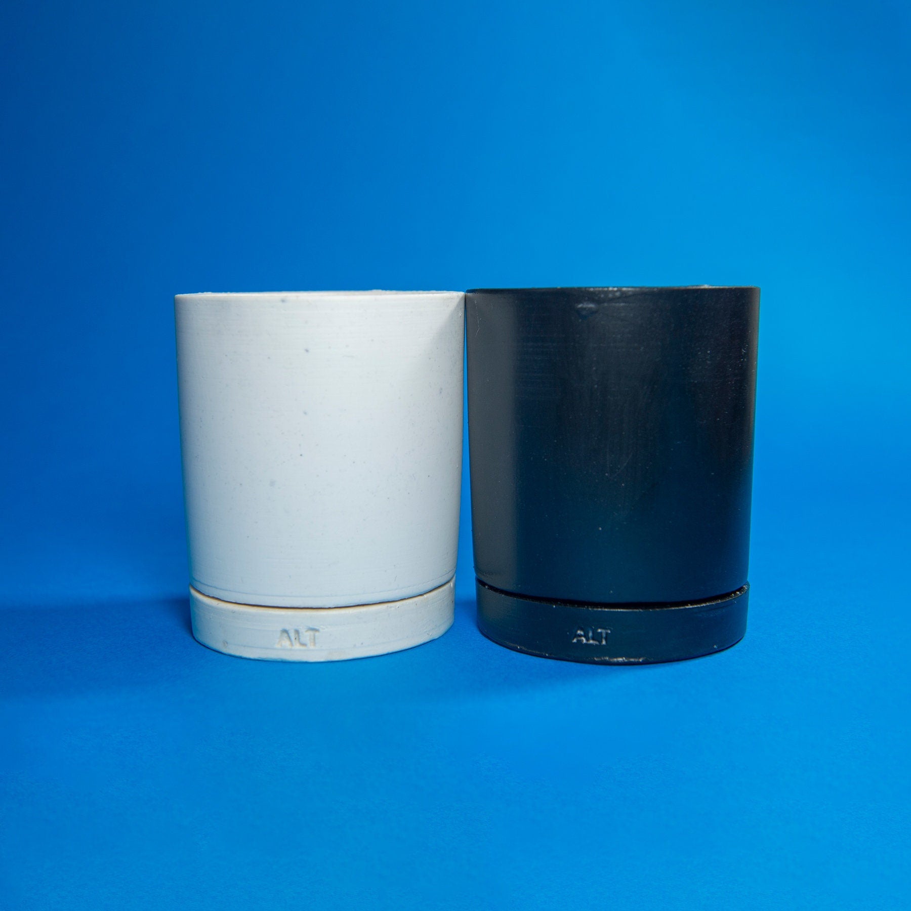 Two cylindrical containers, one white and one black, on a blue background.