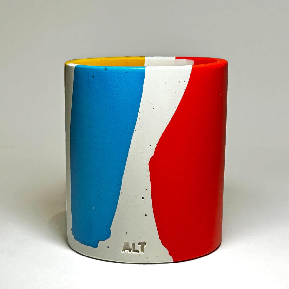 A pen pot with blue, red, and yellow colour block design on a white background