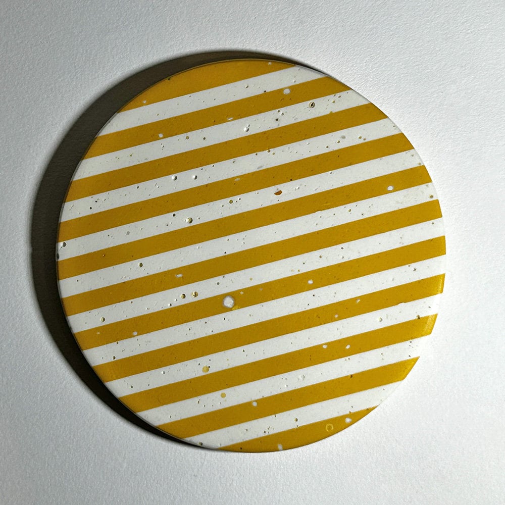 Round coaster with yellow and white striped pattern on a grey background