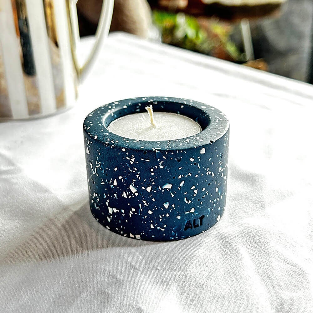 Navy blue terrazzo-patterned tealight candle holder with a white candle inside on a white surface in a living room