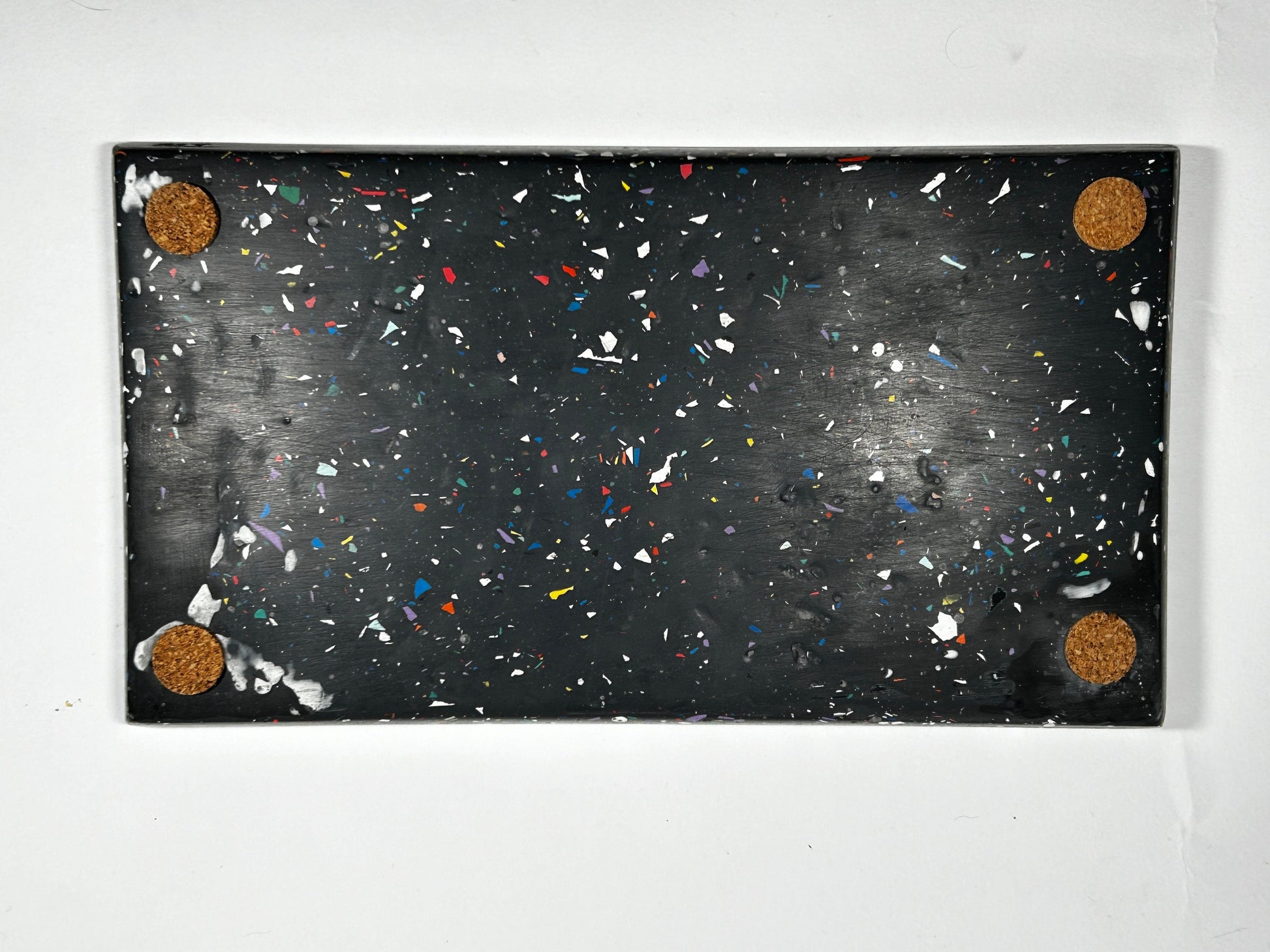 Black speckled tray with colourful terrazzo and four circular brown corks on a white background