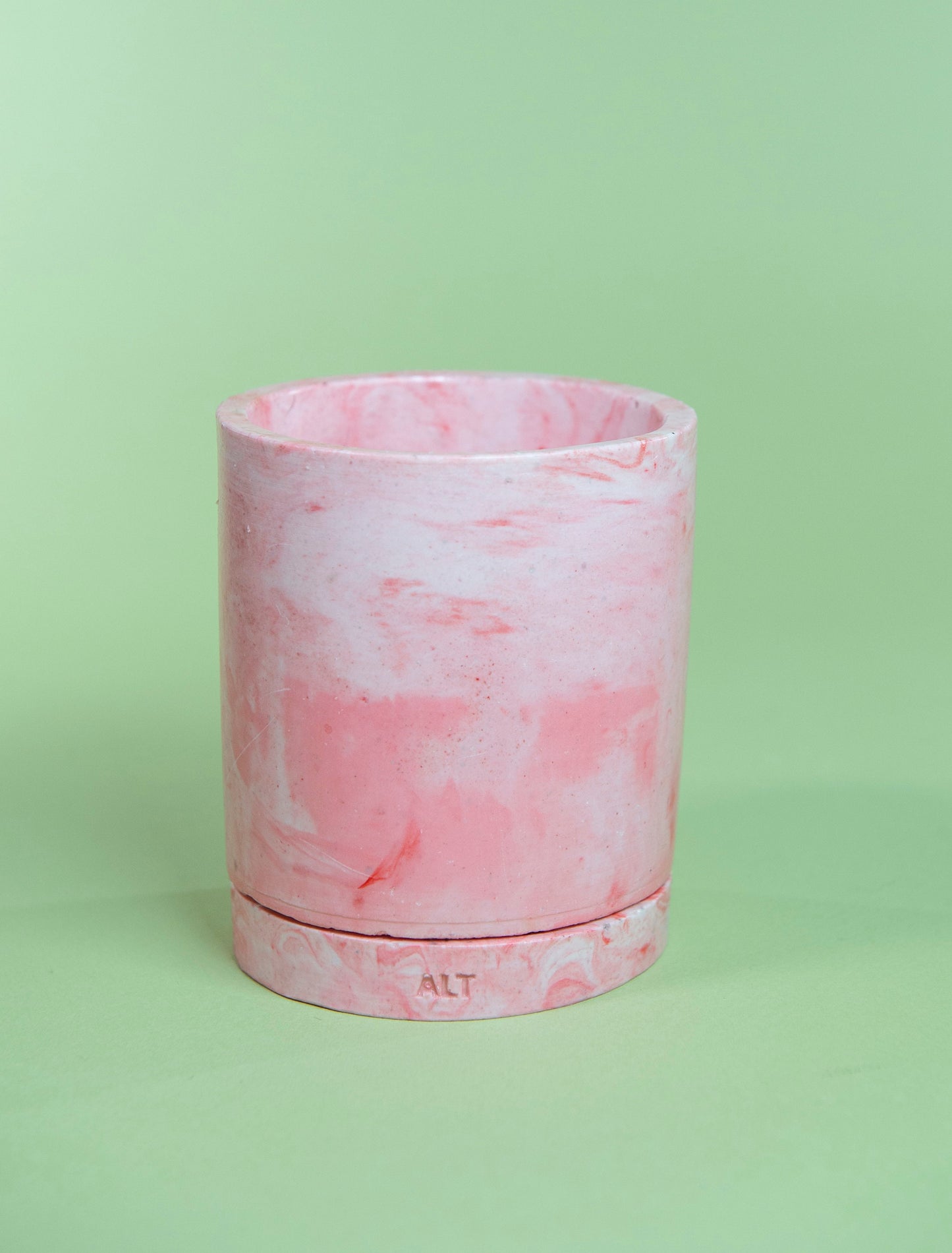 Pink marbled cylindrical plant pot with a drainage and a water tray on a green background