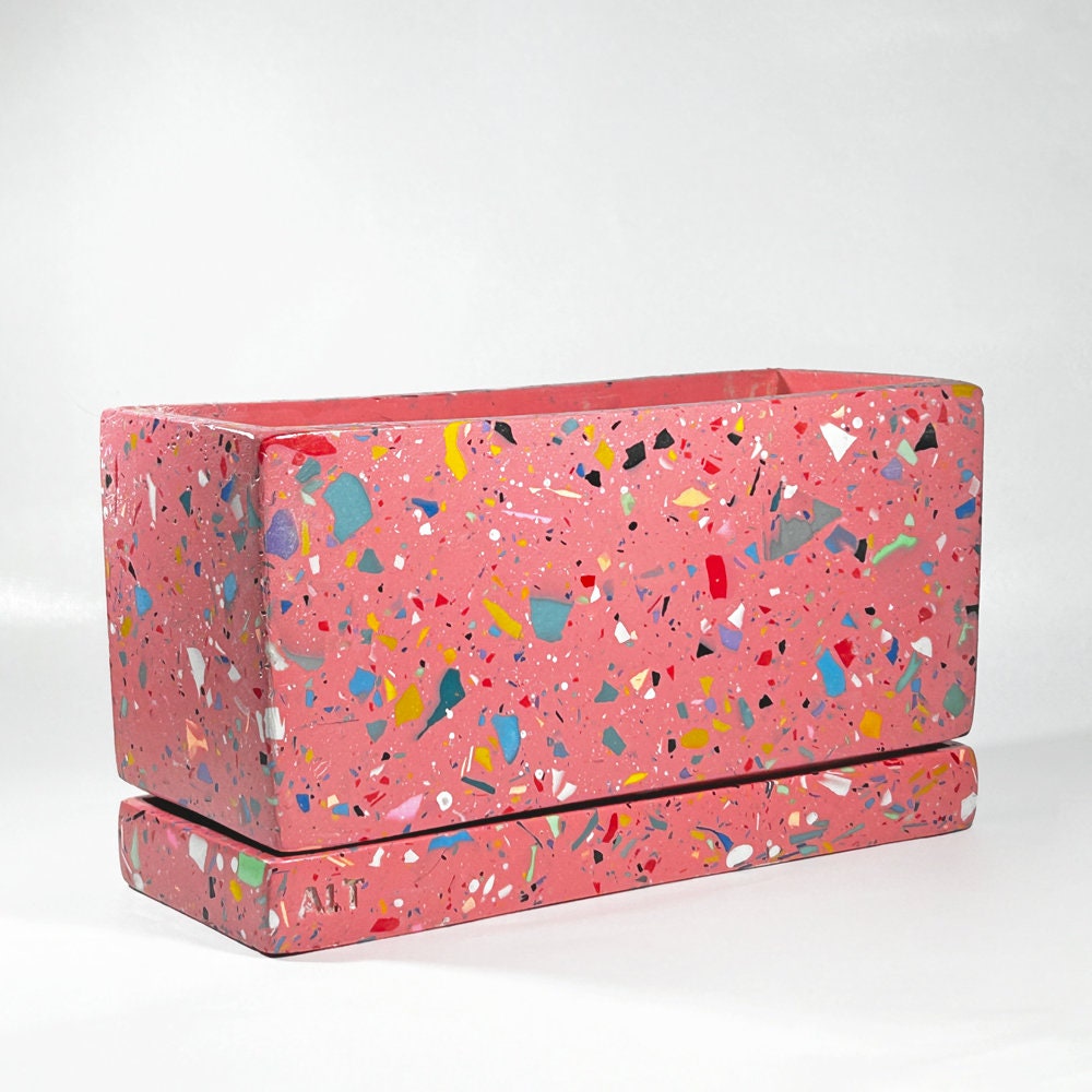 Pink rectangular plant pot with colourful speckles terrazzo with drainage holes and a water tray on a white background