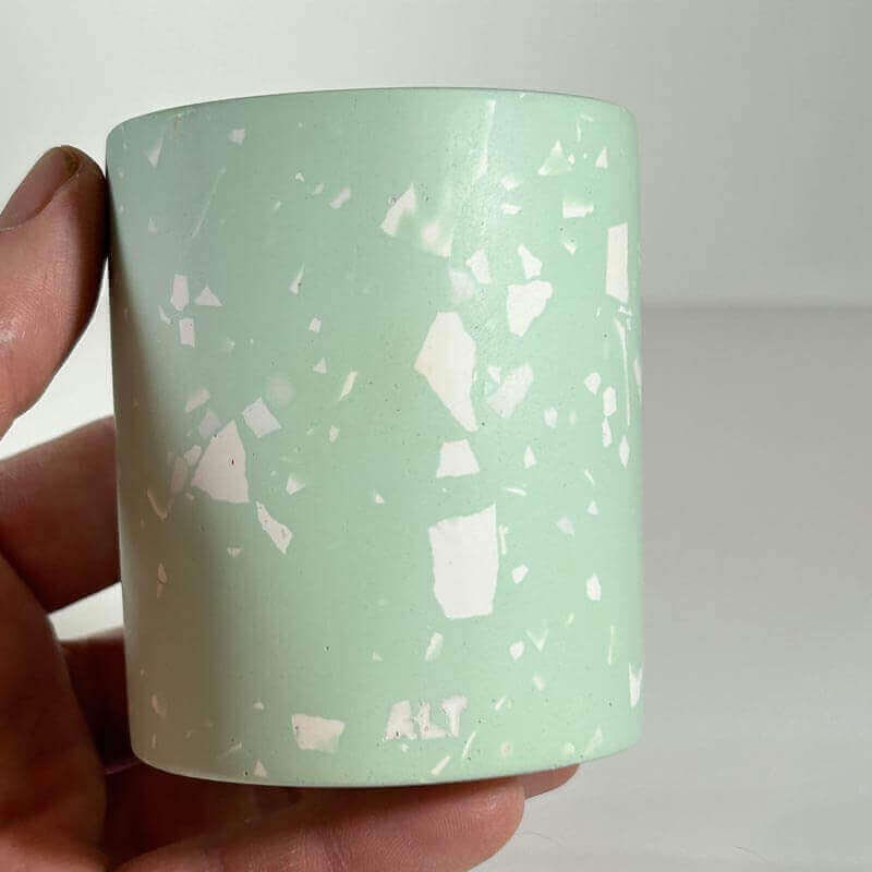 Hand holding a mint green pen pot with white speckles on a plain background