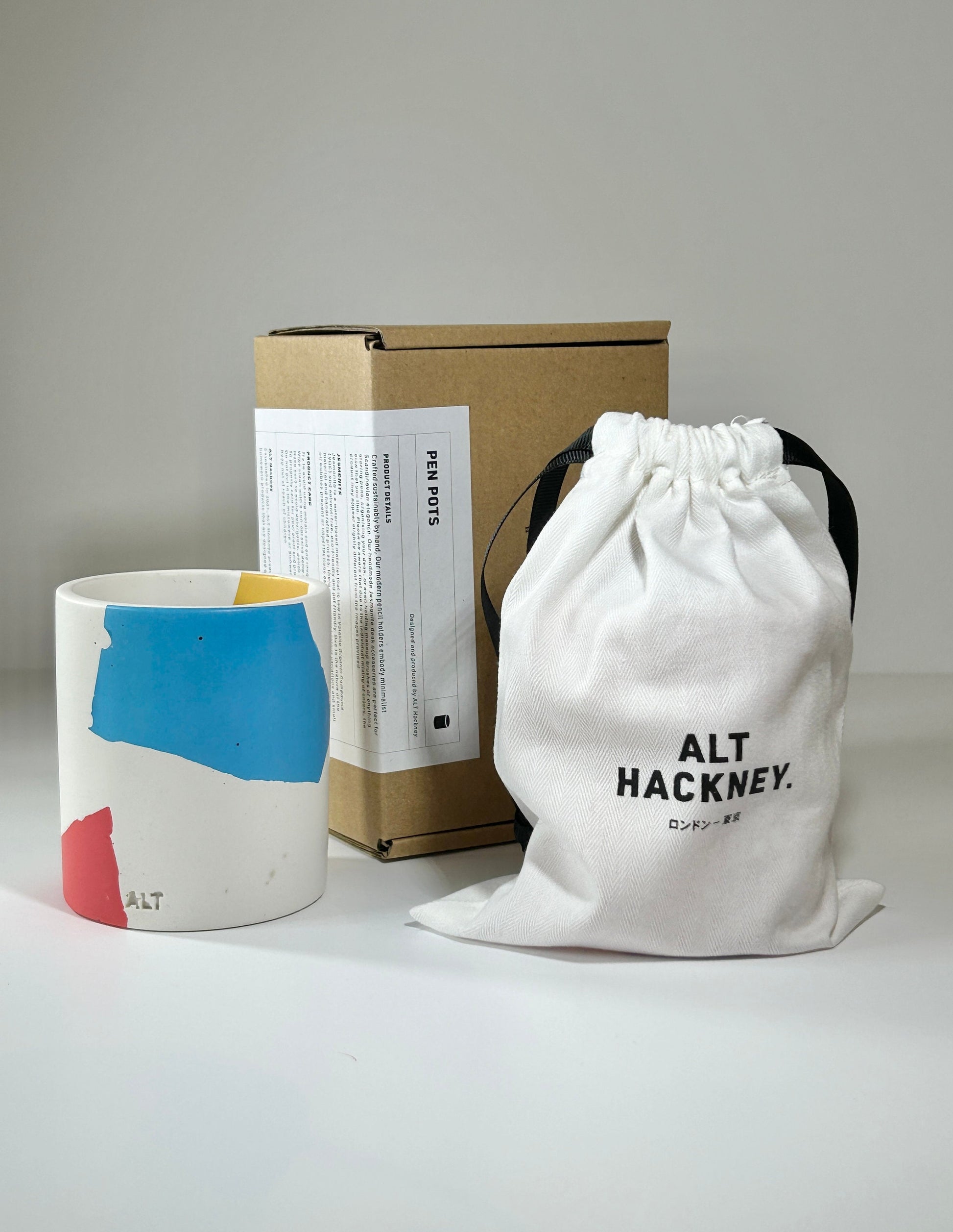 Pen pot with colourful design, branded box, and drawstring bag on a light grey background