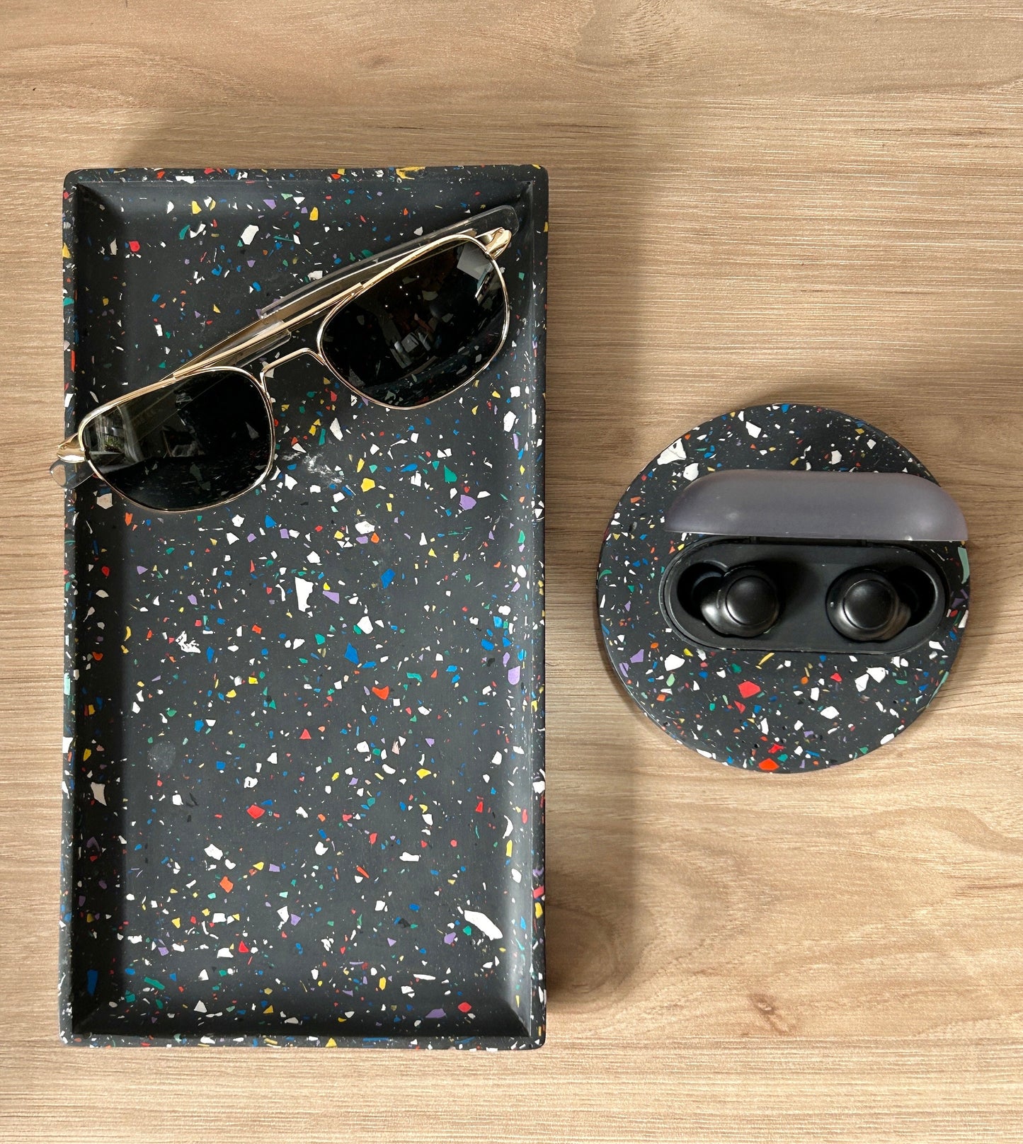 Terrazzo black case with sunglasses and speckled coaster with earbuds on a wooden surface