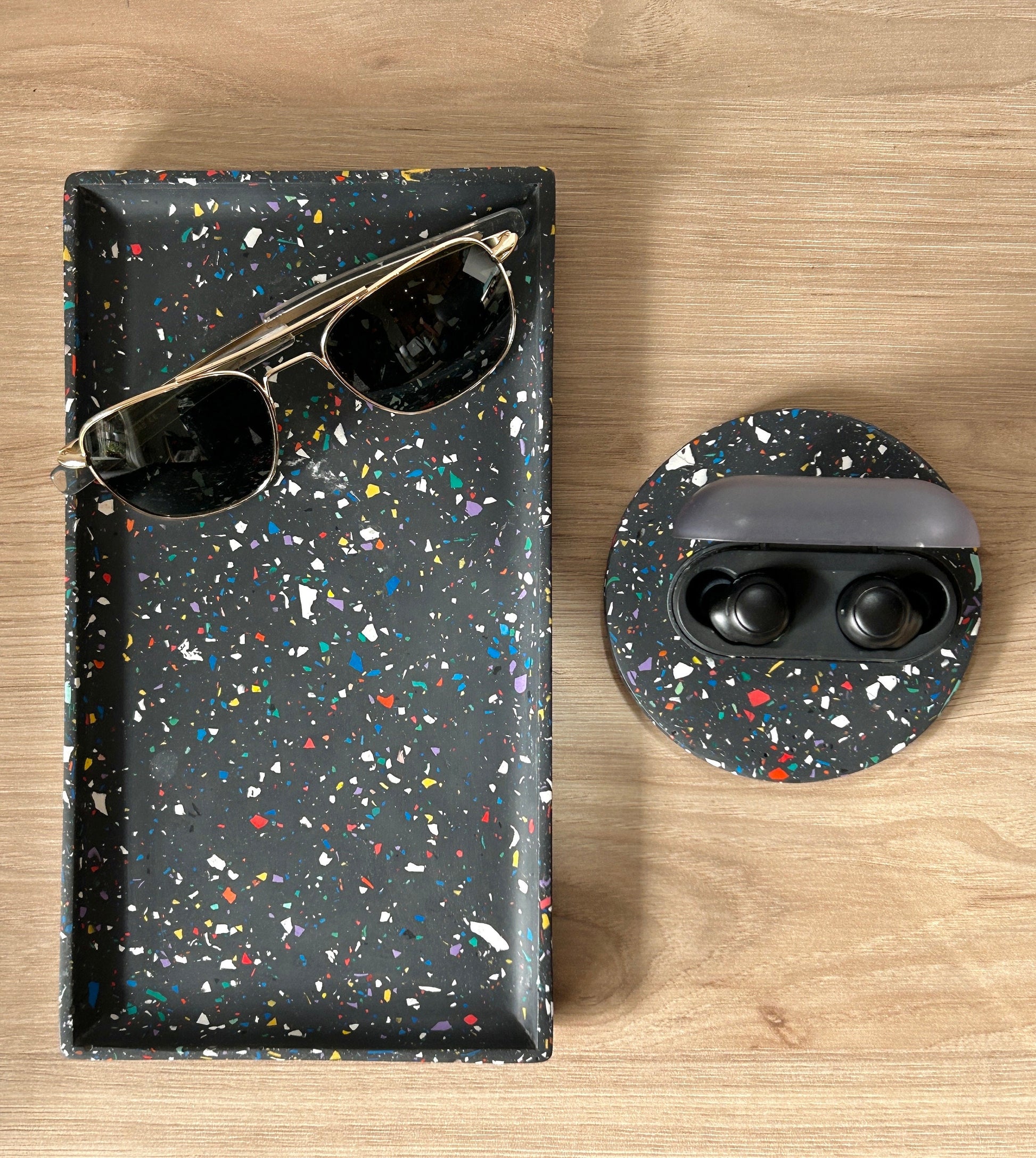 Terrazzo black case with sunglasses and speckled coaster with earbuds on a wooden surface