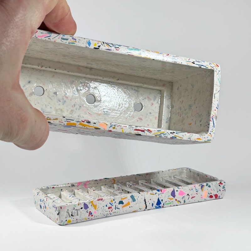 Colorful speckled rectangular container with a hand holding it open on a white background