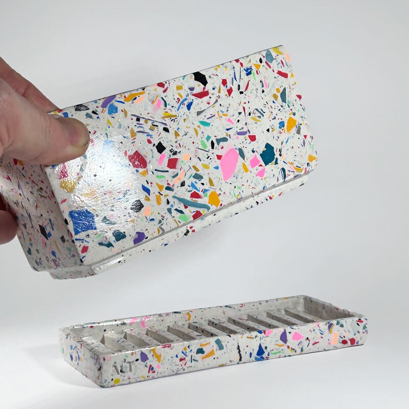 Colorful terrazzo-patterned phone case with a hand holding it open on a white background
