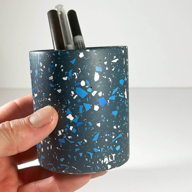 Hand holding a blue and white speckled pen holder with pens inside on a white background