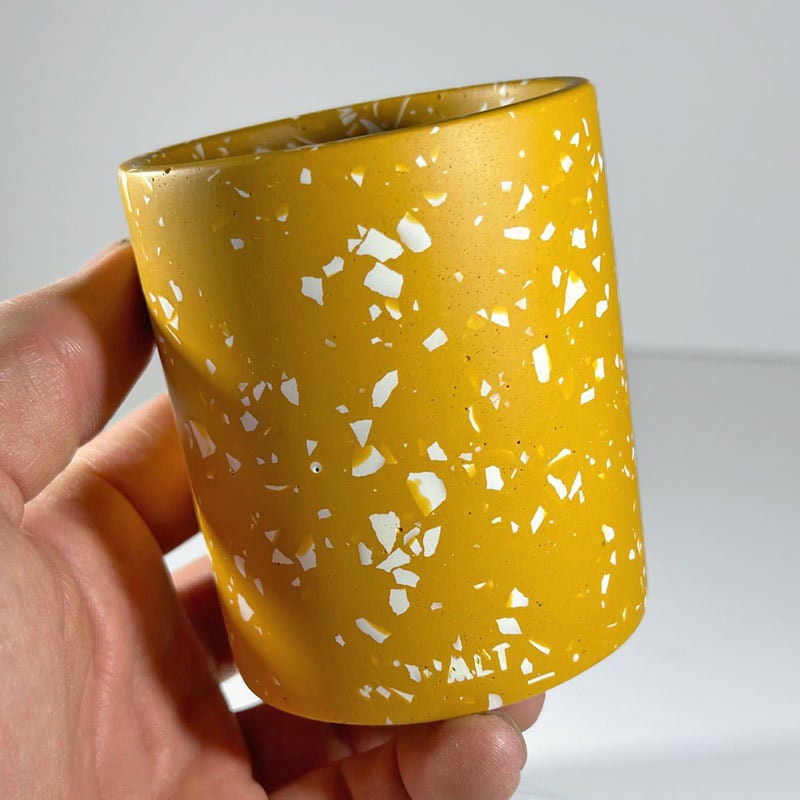 Yellow pen pot with white speckles held by a hand against a light grey background