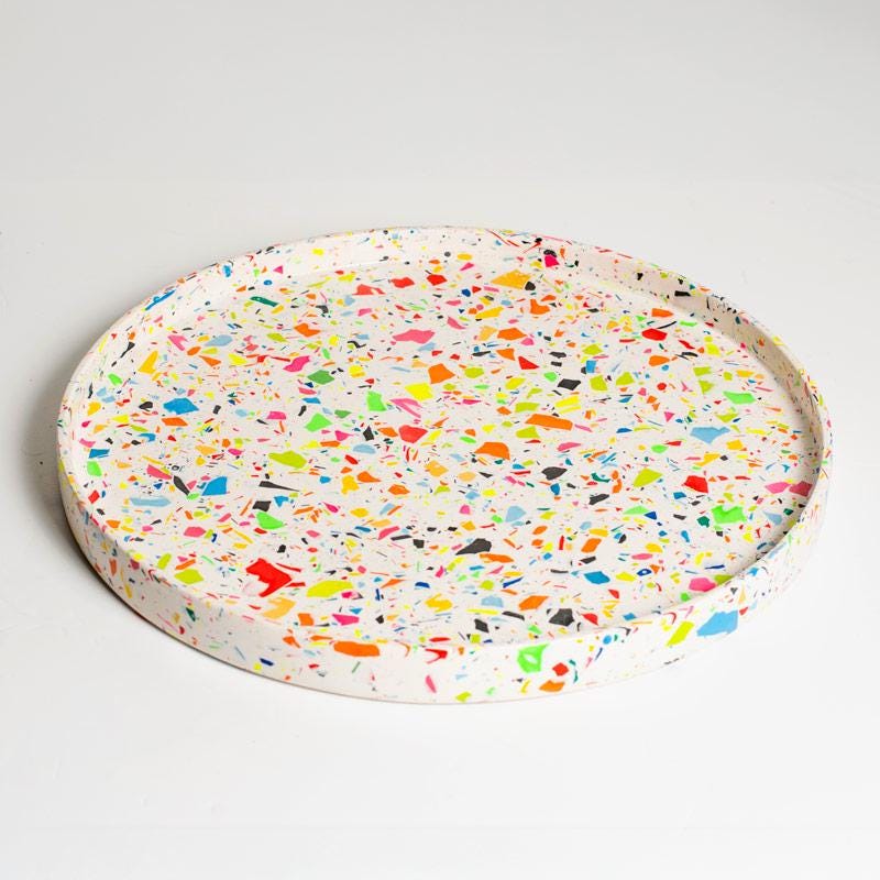 Round terrazzo-style coaster with multicolored speckles on a light gray background