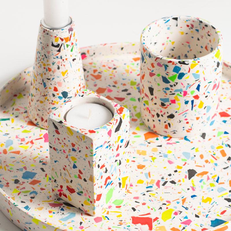 Colourful terrazzo-patterned candles holders and a pen pot  on a decorative tray on a white background