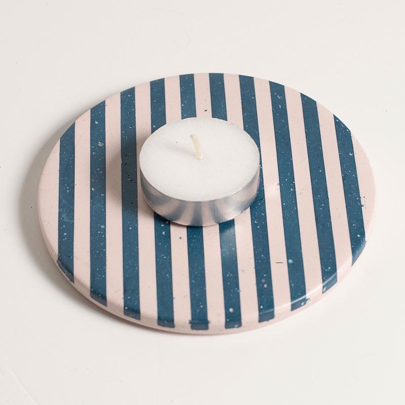 A tea light on a blue and light pink checkered coaster on a white background