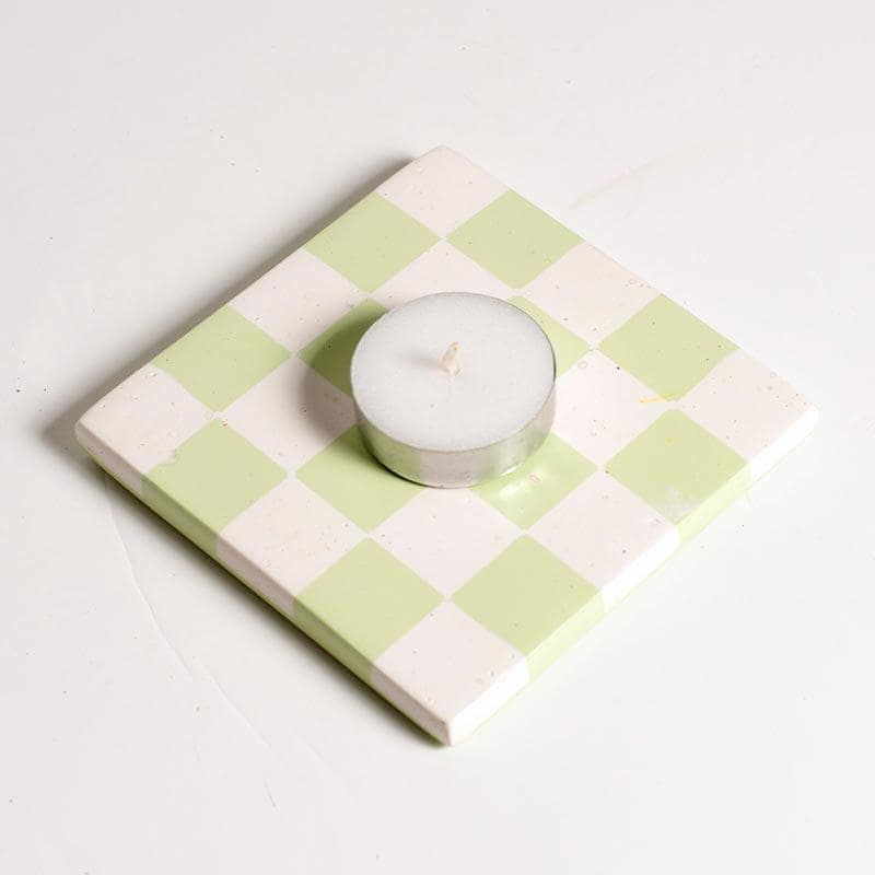 Tealight candle on a checkered coaster with mint green and white squares.