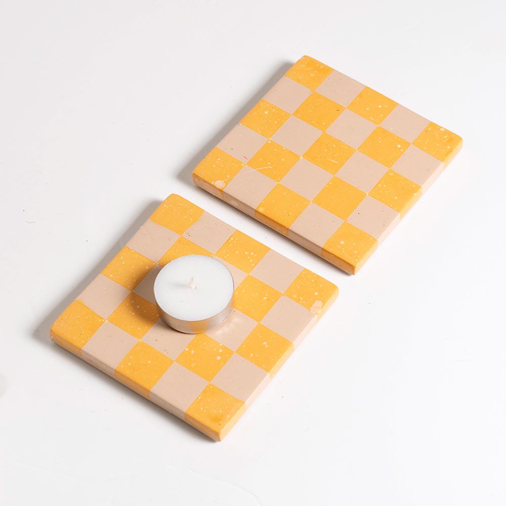 Two checkered coasters with a candle on a light grey background