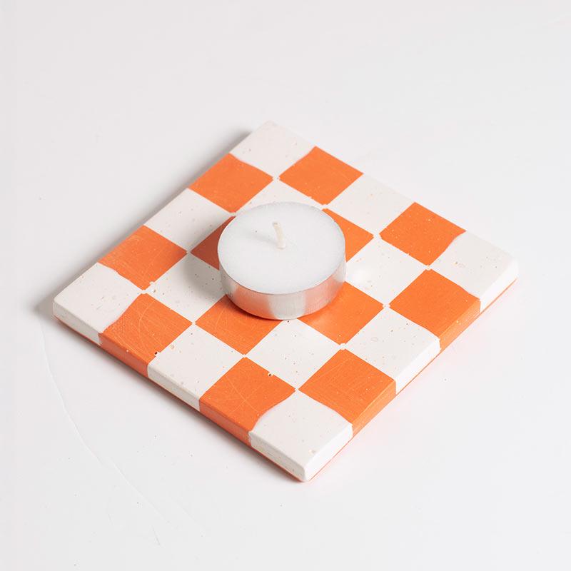 Checkered coasters with orange and white with a tea light on a light grey background