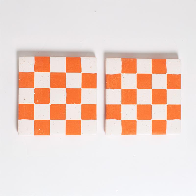 Two checkered coasters with orange and white squares on a light grey background