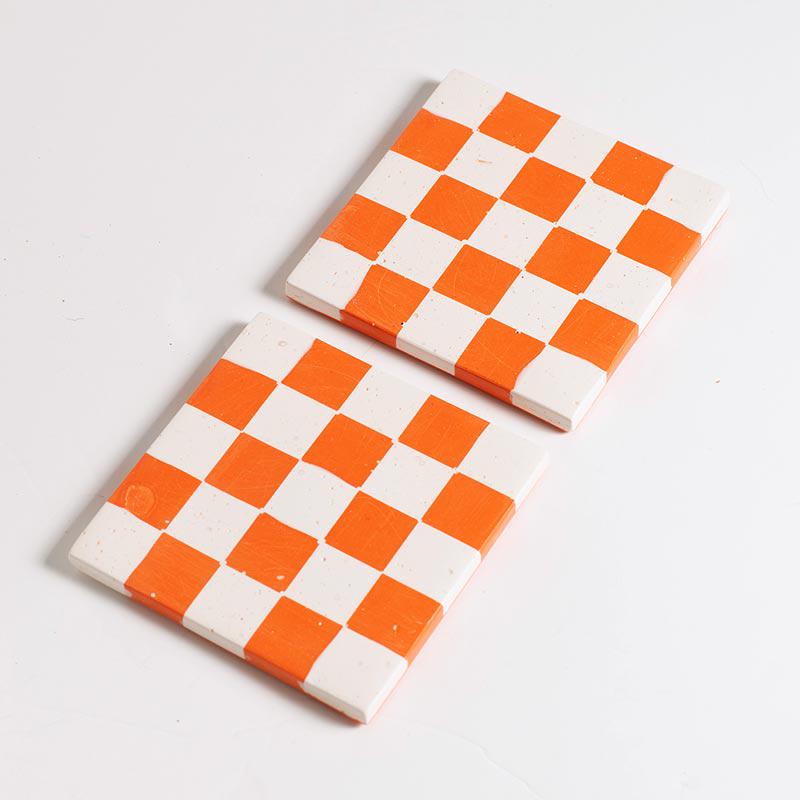 Two checkered coasters with orange and white squares on a light grey background