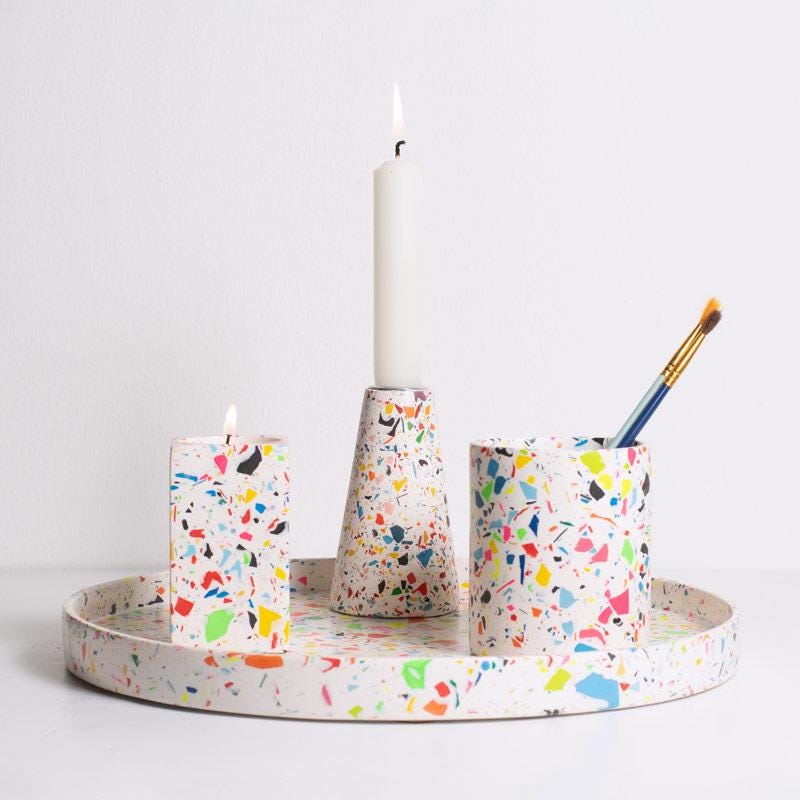 Colourful rainbow terrazzo-patterned candle holders and pen pot with paint brushes on a decorative round tray on a white background