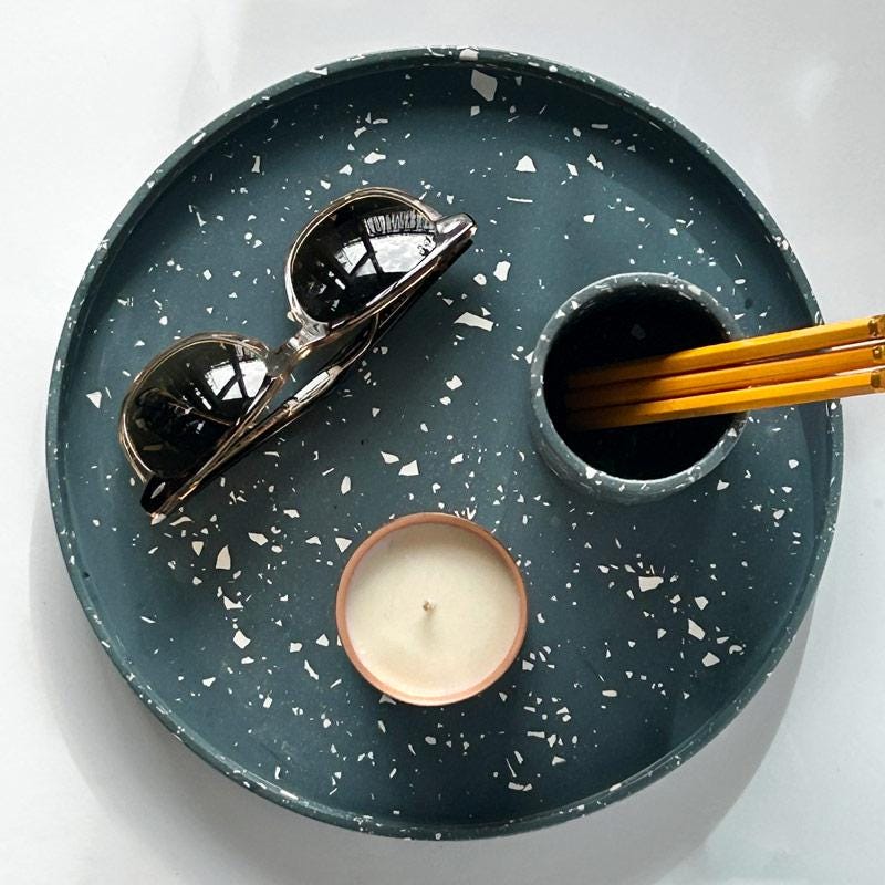 Round navy terrazzo tray with sunglasses, candle, and container on a white background
