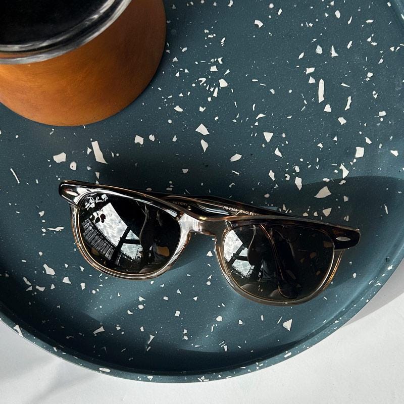 Sunglasses on a navy blue terrazzo tray with a brown diffuser in the corner