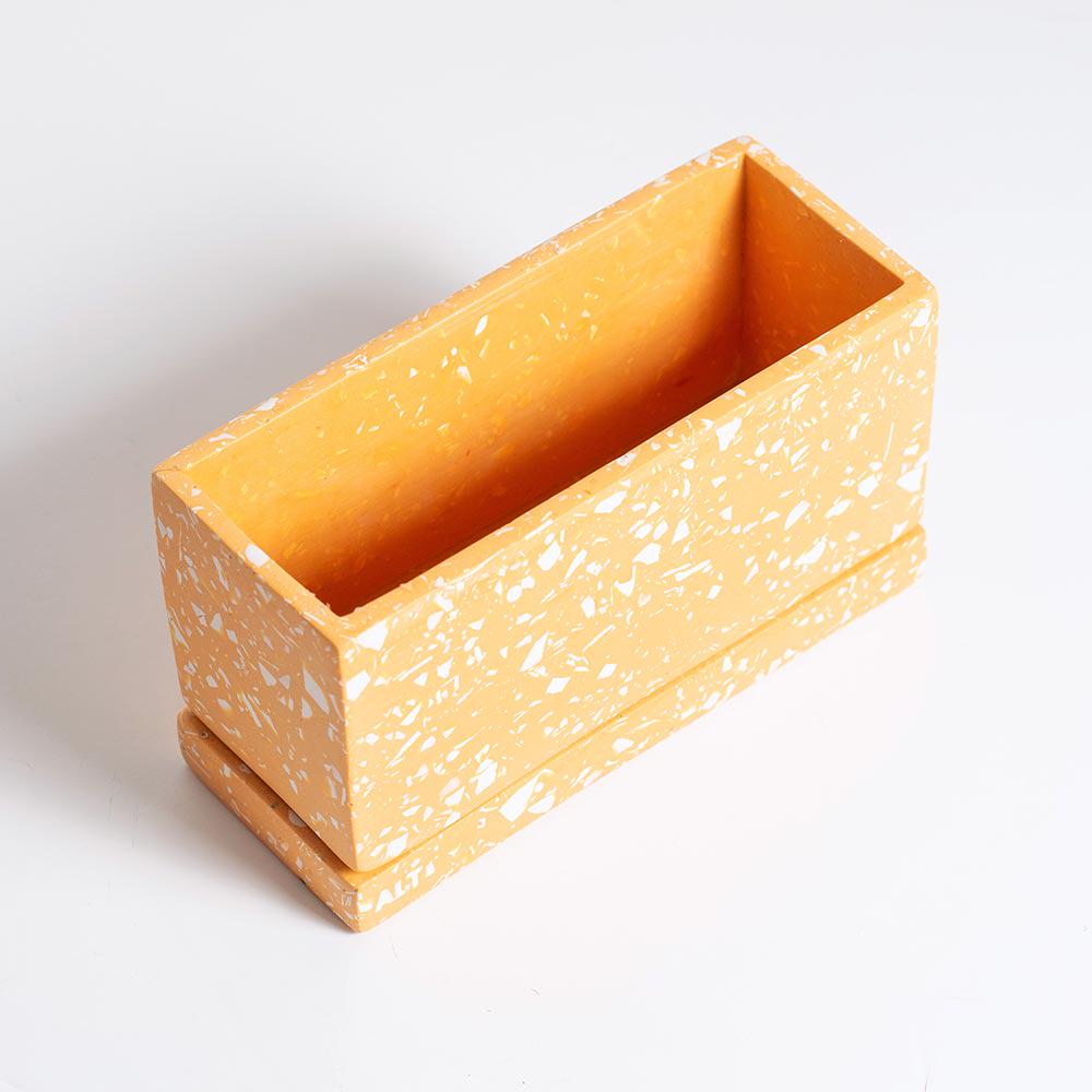 Orange rectangular terrazzo planter with drainage holes and a water tray on a white background