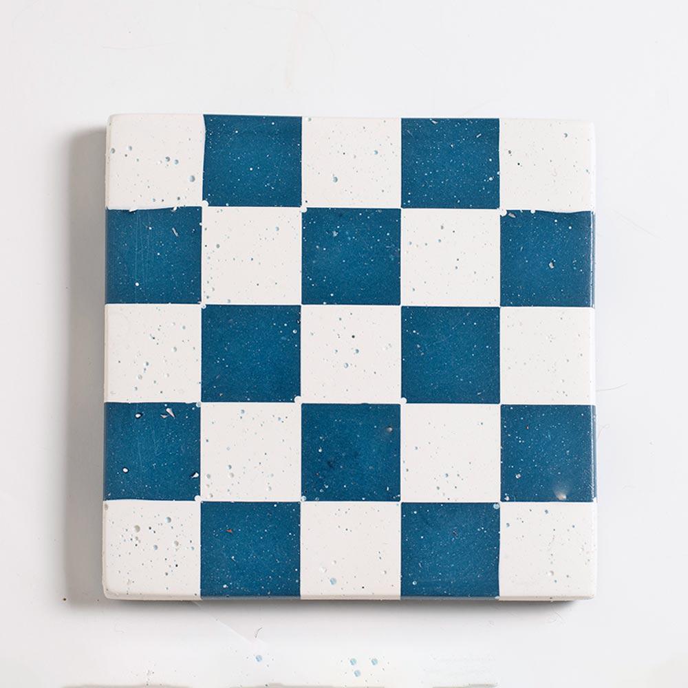 Checkered pattern with blue and white square coaster on a light grey background