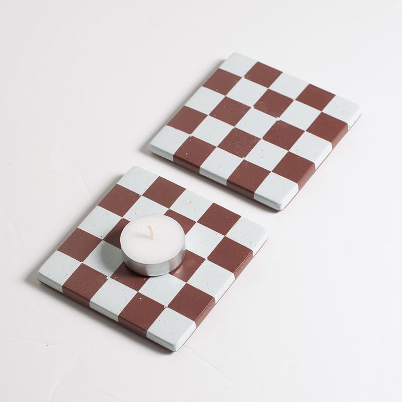 Two checkered coasters with a candle on a light gray background