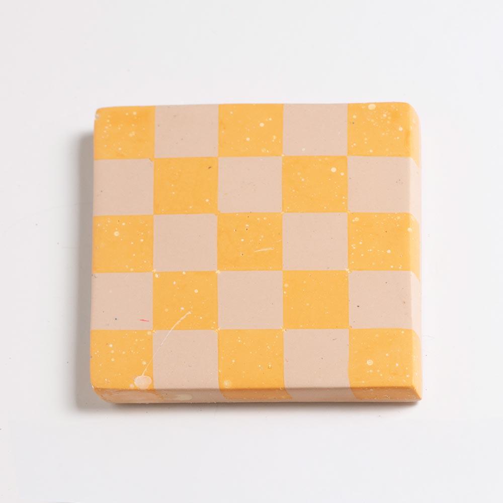 Yellow and beige checkered coaster on a light grey background