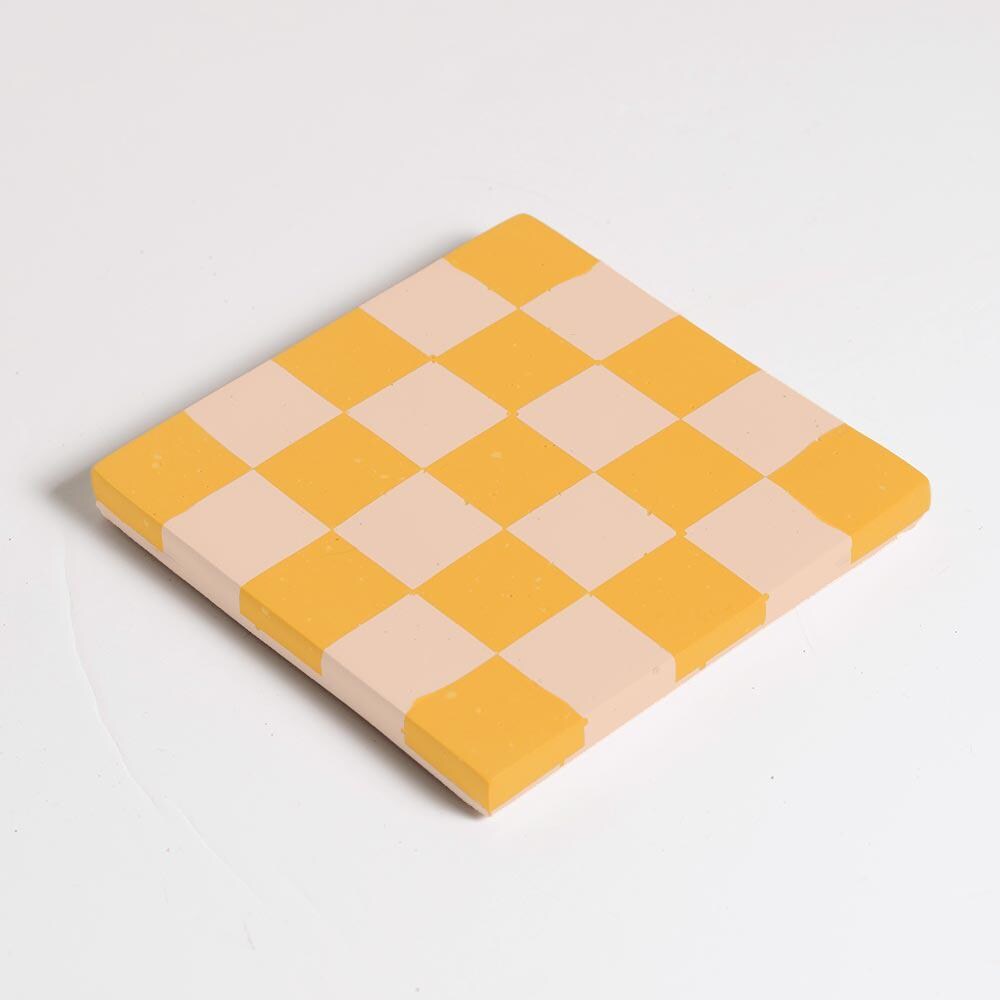 Yellow and beige checkered coaster on a light grey background