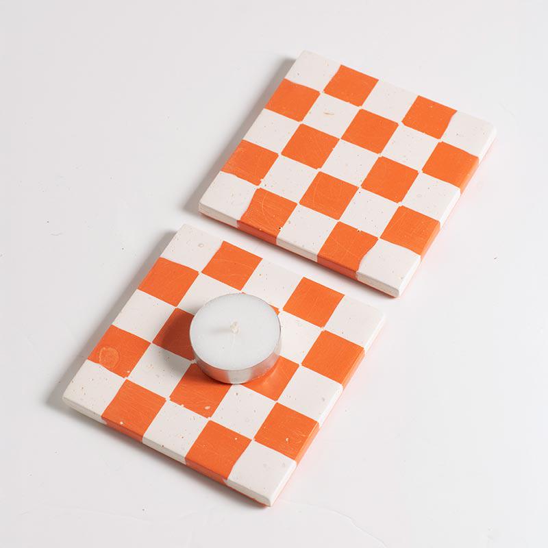 Two checkered coasters with a candle on a light grey background