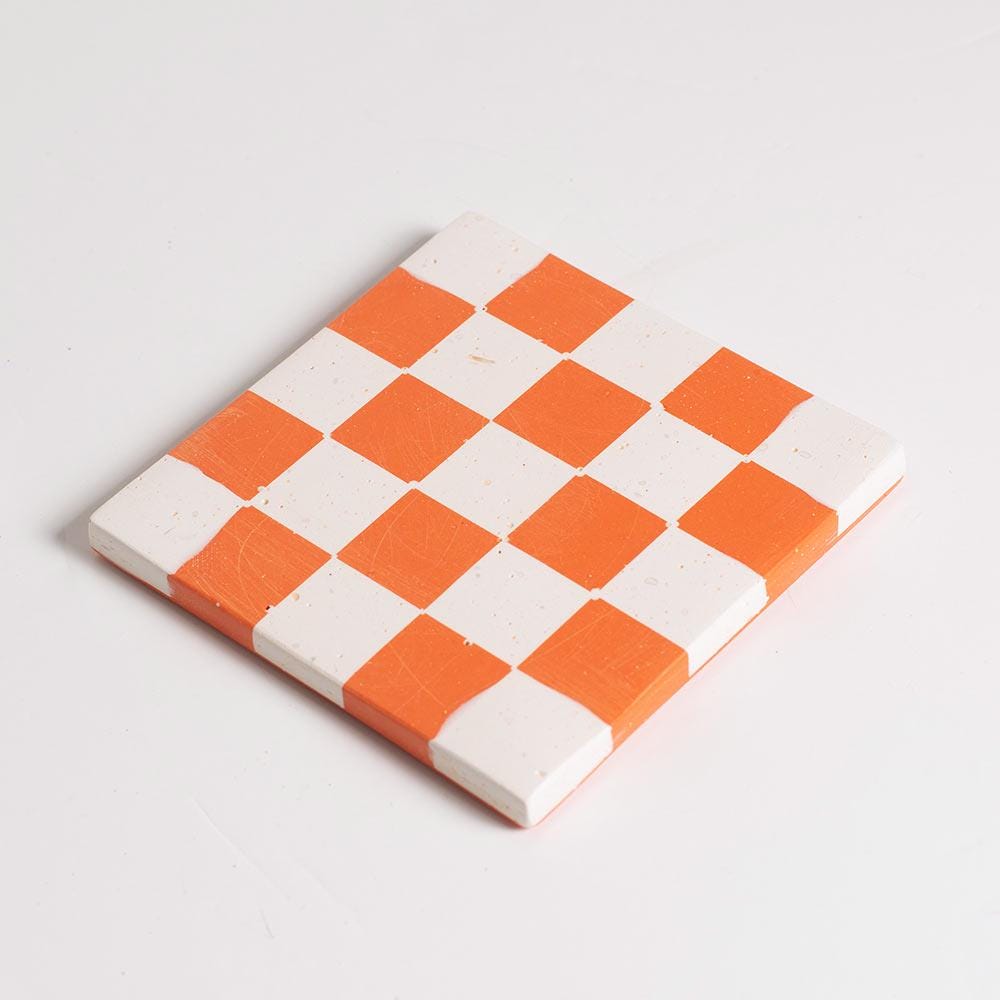Checkered coaster with orange and white squares on a light grey background