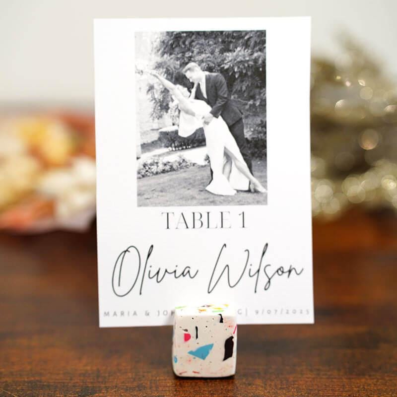 Table name card with a photo of a couple and text 'Olivia Wilson' on a wooden surface.