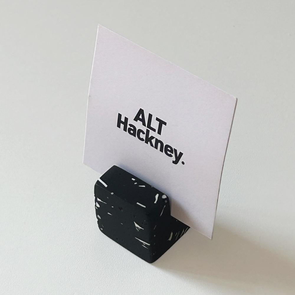 Black cube-shaped card holder with a white card displaying 'ALT Hackney.' text on a light gray background.