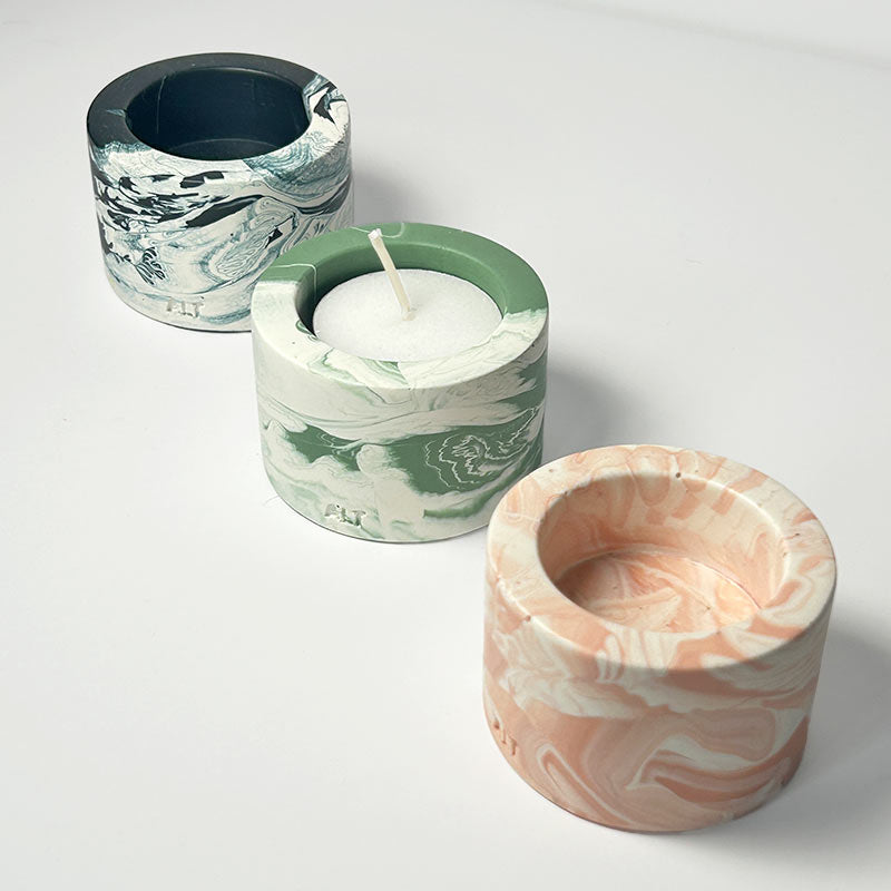 Three marbled-patterned  tealight candle holders with a candle on a white background