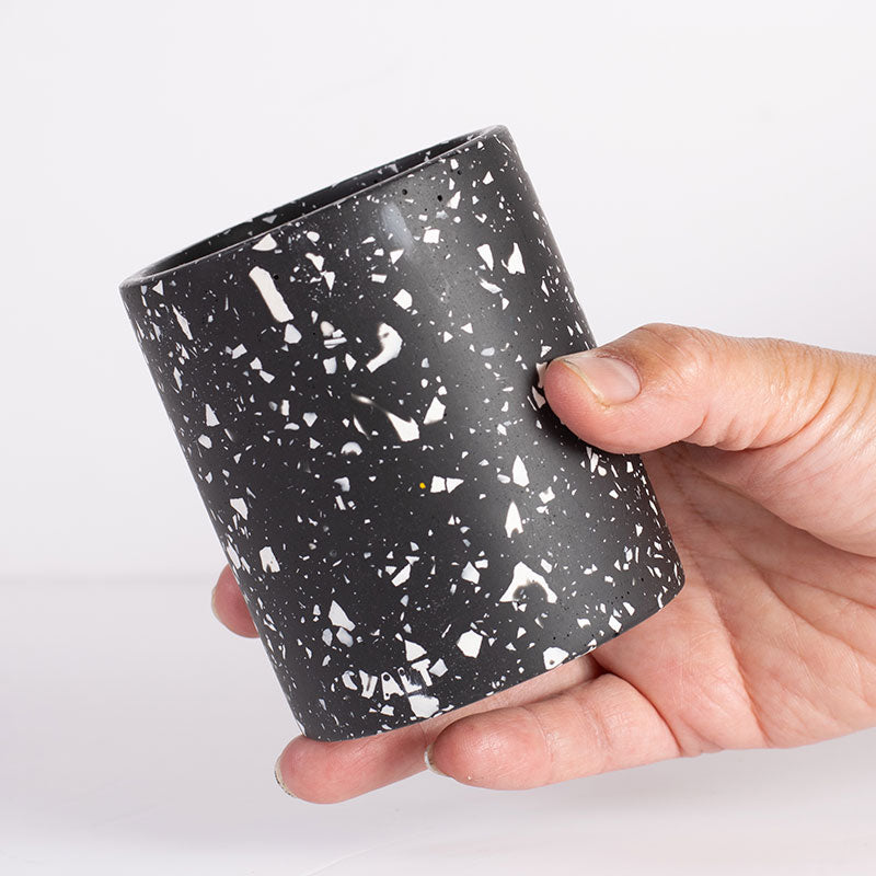 Hand holding a black and white terrazzo pen pot on a white background