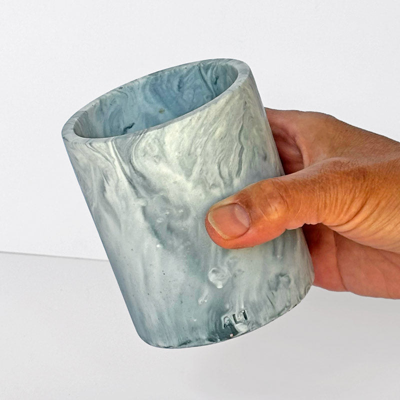 Marble-patterned pen pot with 'ALT' branding held by a hand on a white background