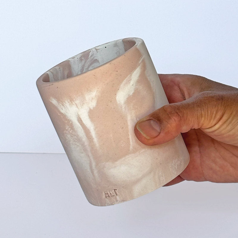 Marble-patterned salmon pink pen pot with 'ALT' branding held by a hand on a white background