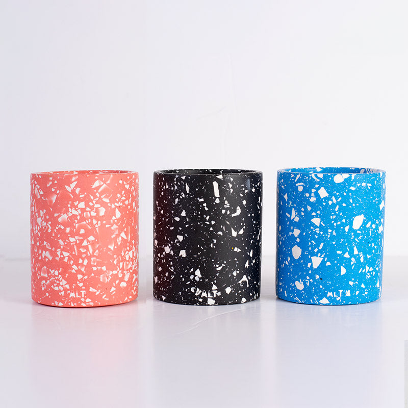Three terrazzo pen pots in pink, black, and blue on a white background