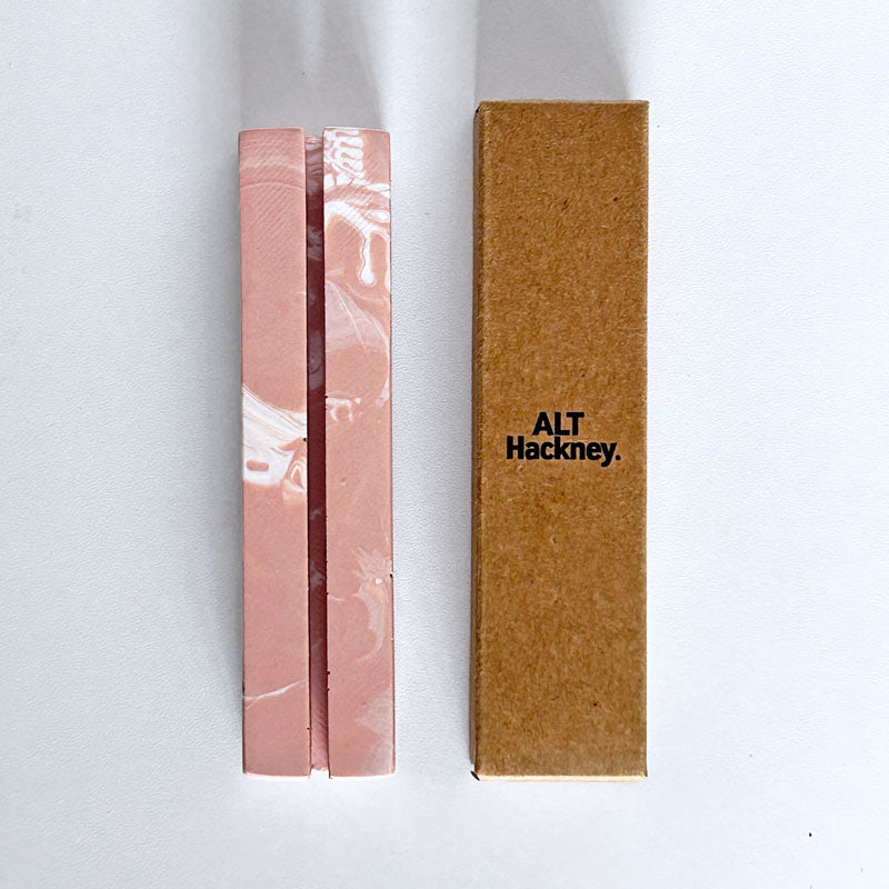 Marble-patterned salmon pink and white photo holder and an eco brown box with 'ALT Hackney' branding, on a white background.