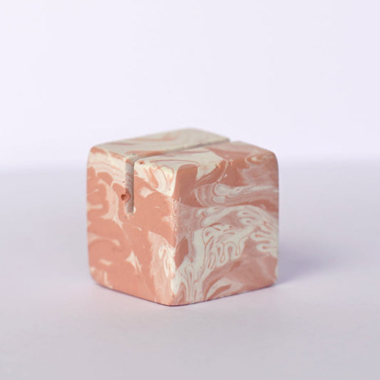 Marble patterned salmon pink small square and white photo holder on a light grey background